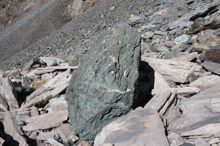 Un bloc de roche verte au milieu de rocailles de marbre et d’autres.